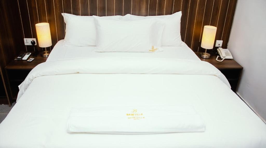 拉各斯Baseville Hotel的一张带白色床单的床和两个带灯的床头柜