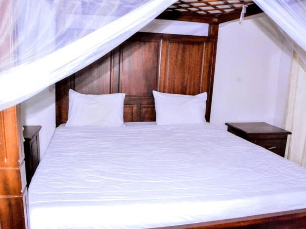 基加利KEZA Home的卧室配有白色的床和木制床头板
