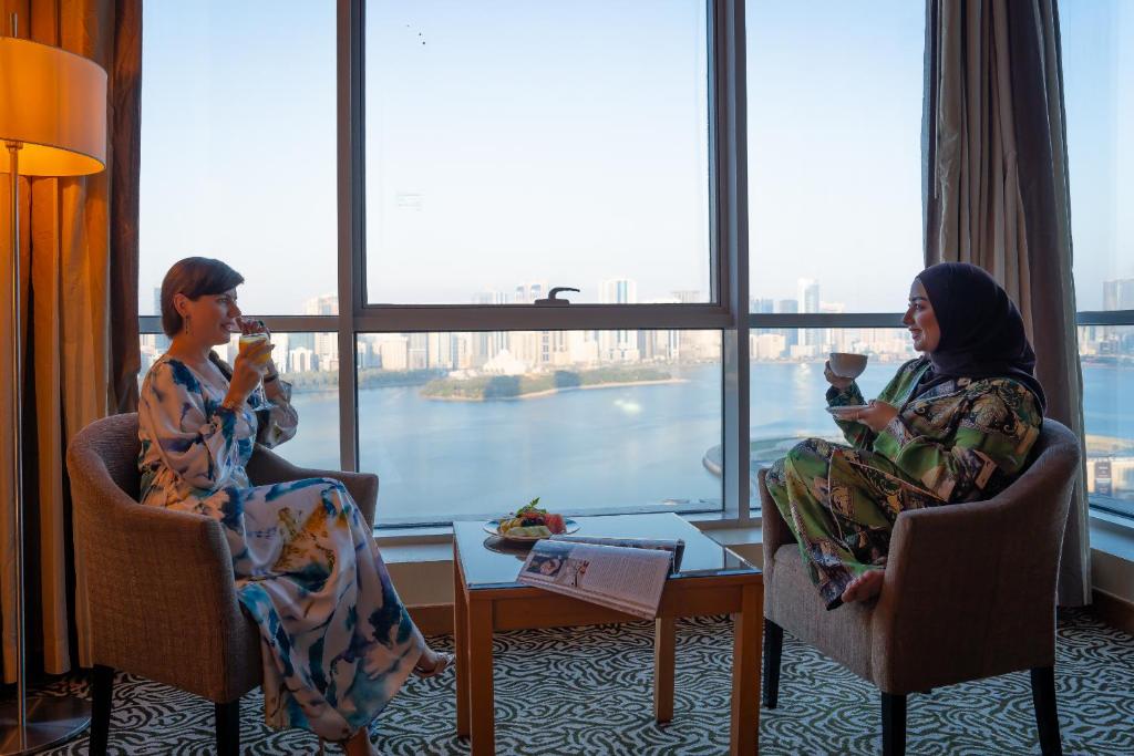 沙迦沙迦国敦大酒店的两个女人坐在椅子上喝着饮料