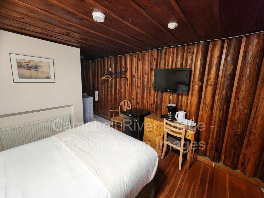 坎贝尔河Campbell River Lodge的一间带木墙的卧室、一张床和电视