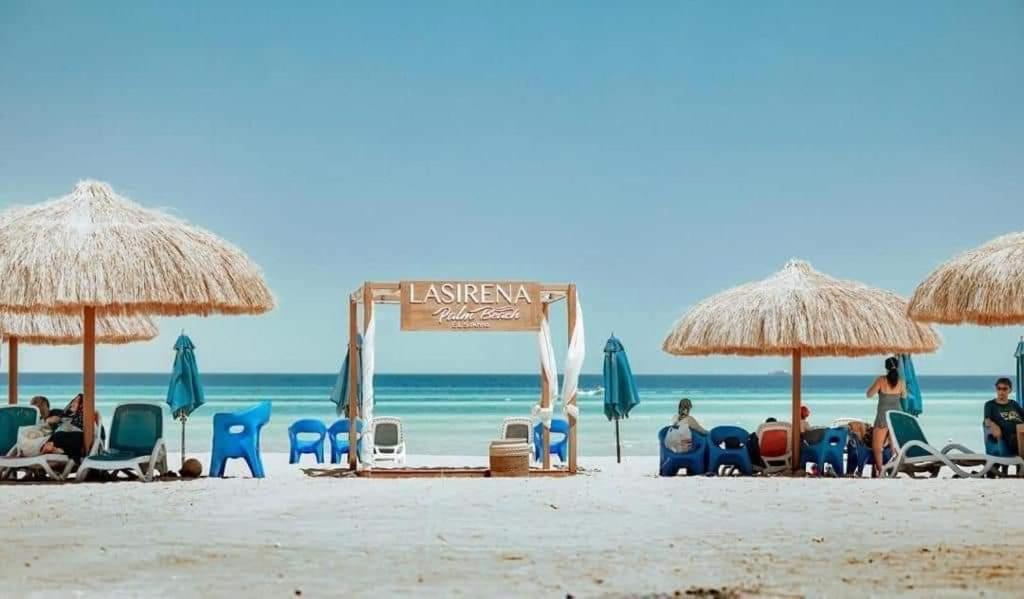 艾因苏赫纳LASIRENA PALM BEACH RESORT -FAMILY的一群人在海滩上,带椅子和遮阳伞