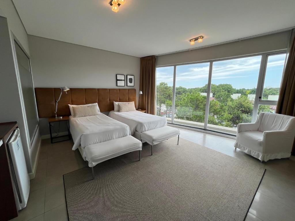 皮纳马尔Hotel Zentiva Pinamar的客房设有两张床、两把椅子和窗户。