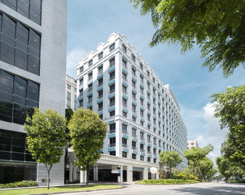 新加坡Adina Serviced Apartments Singapore Orchard的一座高大的白色建筑,前面有树木