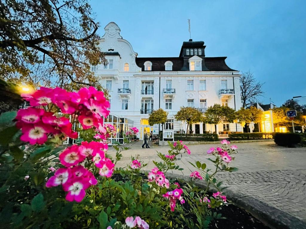 巴特维尔东根昆兰霍夫戈比酒店的一座白色的大建筑,前面有粉红色的花朵