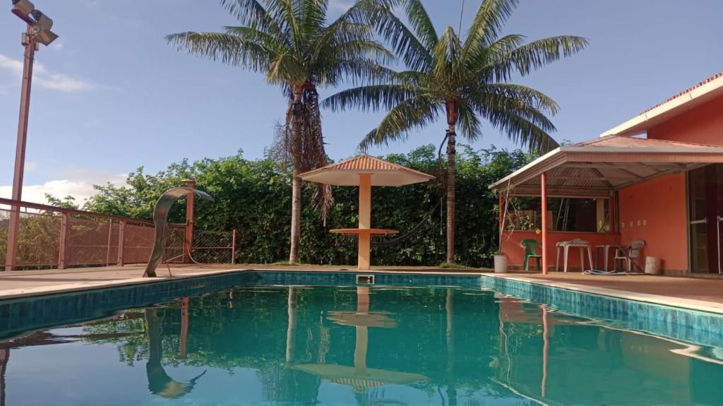 卡皮托利乌Suites Hidromassagem - Pousada Vale da Serra的一个带遮阳伞和棕榈树的游泳池