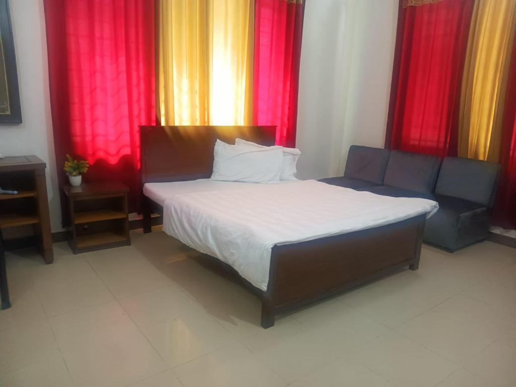 拉瓦尔品第Capital Guest Inn的配有红色窗帘的房间,床和沙发