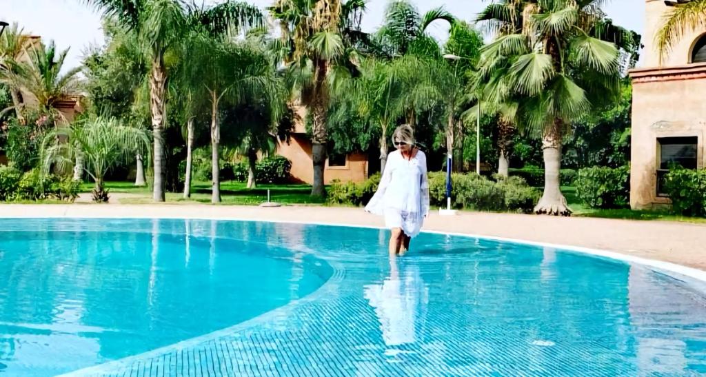 马拉喀什La Perle de l'Atlas by Golf Resort的穿白色衣服的女人走进游泳池
