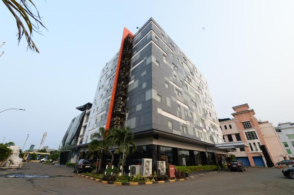 雅加达HORU HOTEL MANGGA DUA SQUARE的一座高大的灰色建筑,前面有棕榈树