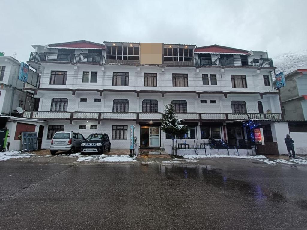 巴德里纳特Hotel Badrinath的一座白色的大建筑,前面有汽车停放