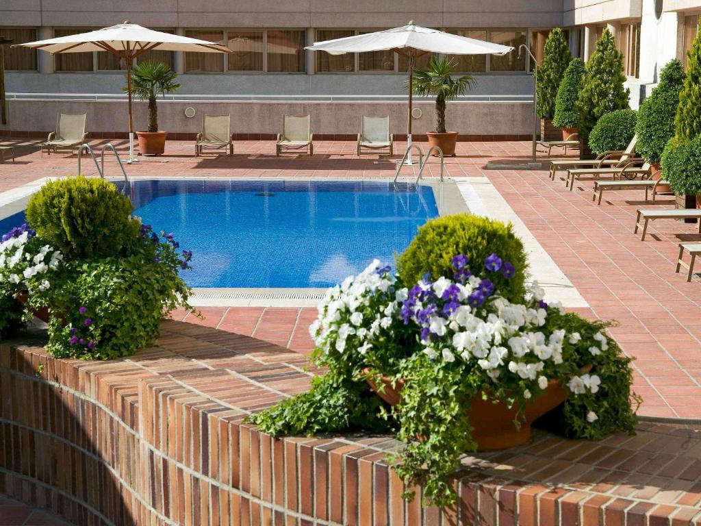 马德里诺富特坎波德拉斯纳西昂酒店的一座带盆栽花卉和桌椅的游泳池