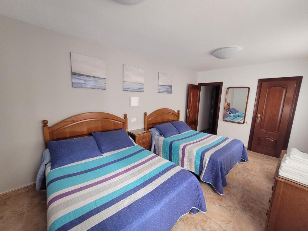 希洪Hostal San Felix的一间卧室配有两张带蓝色和条纹床单的床
