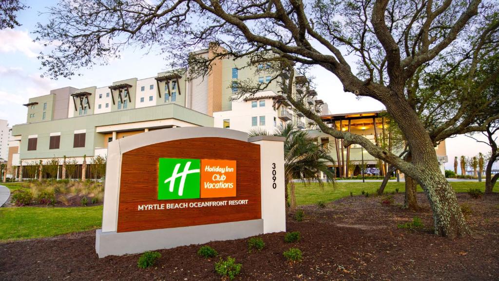 默特尔比奇Holiday Inn Club Vacations Myrtle Beach Oceanfront, an IHG Hotel的一座有树的建筑前面的标志