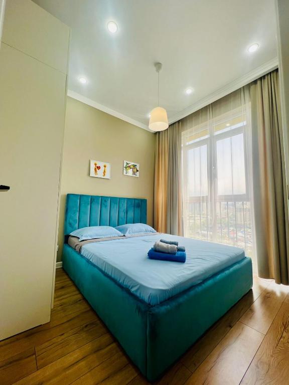 阿拉木图VIP APARTMENT的一张蓝色的床,位于带大窗户的房间里