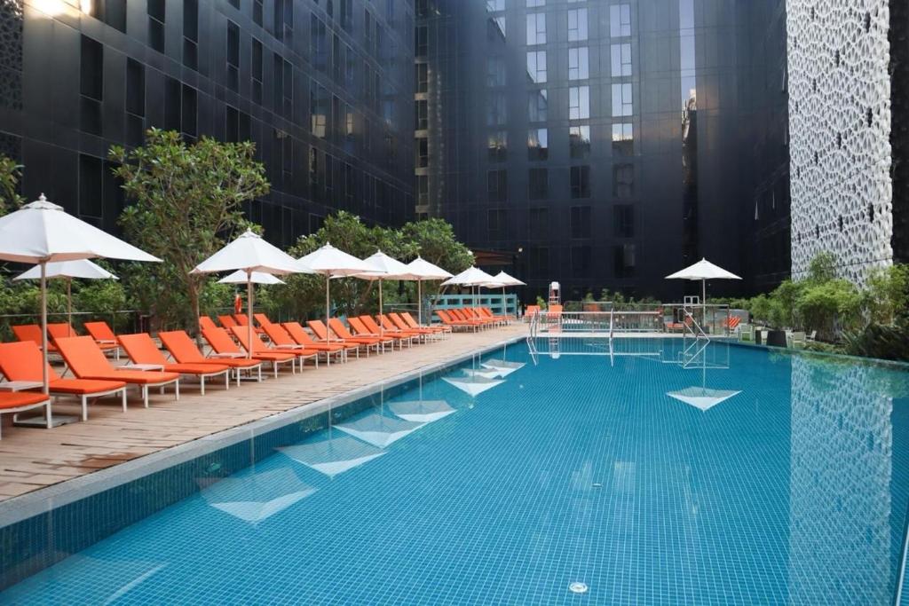 迪拜Grand Mercure Dubai City的一座带橙色椅子和遮阳伞的大型游泳池