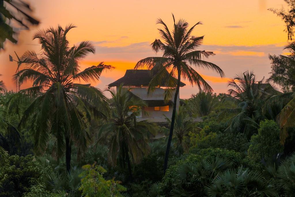 拉穆Pepo Villa, Anasa Hotels & Experiences的日落前有棕榈树的建筑