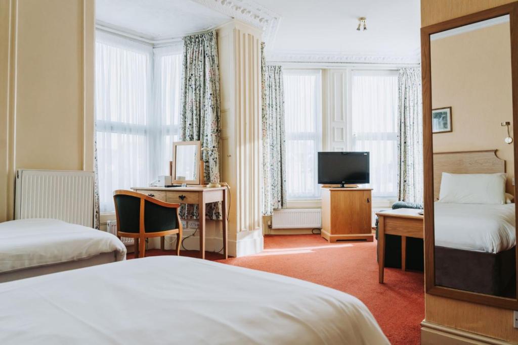 道格拉斯Welbeck Hotel & Apartments的酒店客房设有两张床、一张桌子和一台电视。