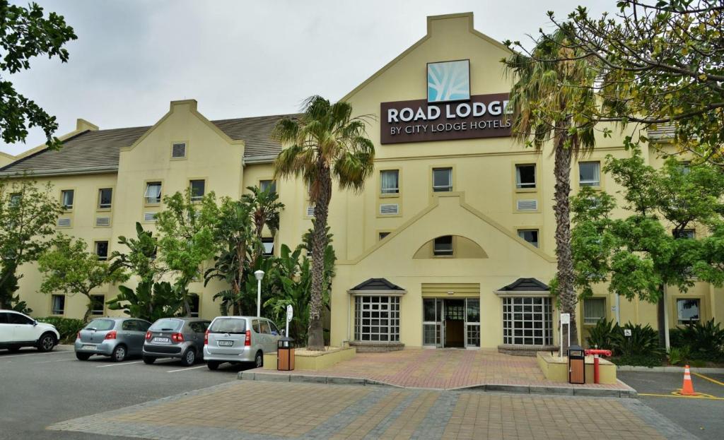 开普敦Road lodge Hotel Cape Town International Airport -Booked Easy的一座黄色的大建筑,前面有汽车停放