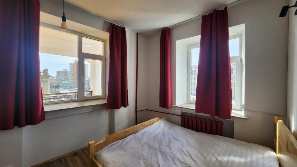 乌兰巴托Ulaanbaatar Hostel的一间卧室配有床和两个带红色窗帘的窗户。