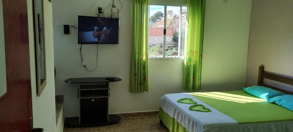 圣托梅-达斯莱特拉斯Kit net montanha mágica的一间卧室配有一张带绿色窗帘的床和电视。