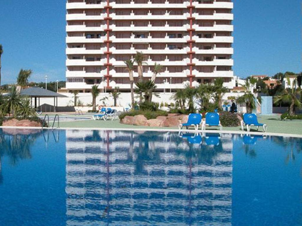 卡尔佩Apartamentos Coral Beach Unitursa的一座带蓝色椅子的游泳池以及一座大型建筑