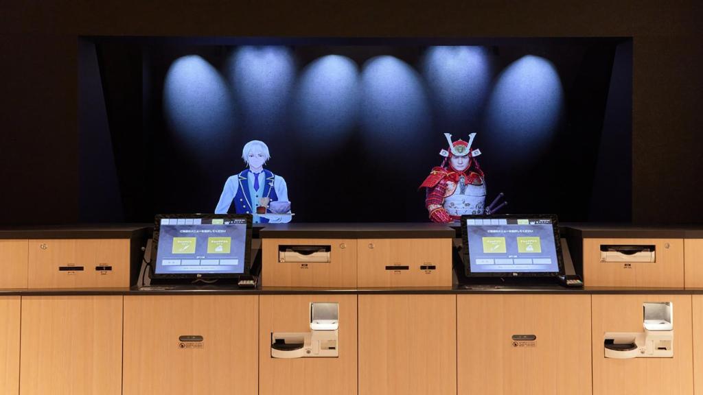 鹿儿岛Henn na Hotel Kagoshima Tenmonkan的一张带男人的电视屏幕和一张桌子上的两台笔记本电脑