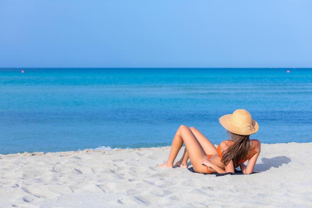 乌真托Riva di Ugento Beach Camping Resort的坐在海滩上的戴帽子的女人
