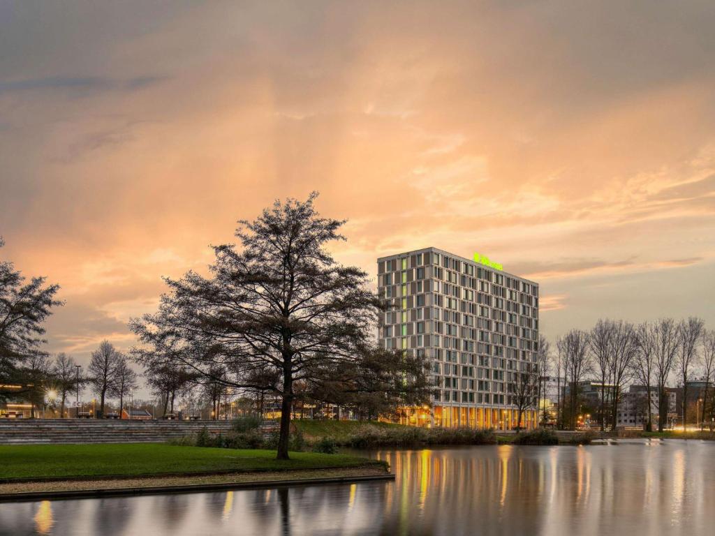 鹿特丹ibis Styles Rotterdam Ahoy的湖前高大的建筑,有树