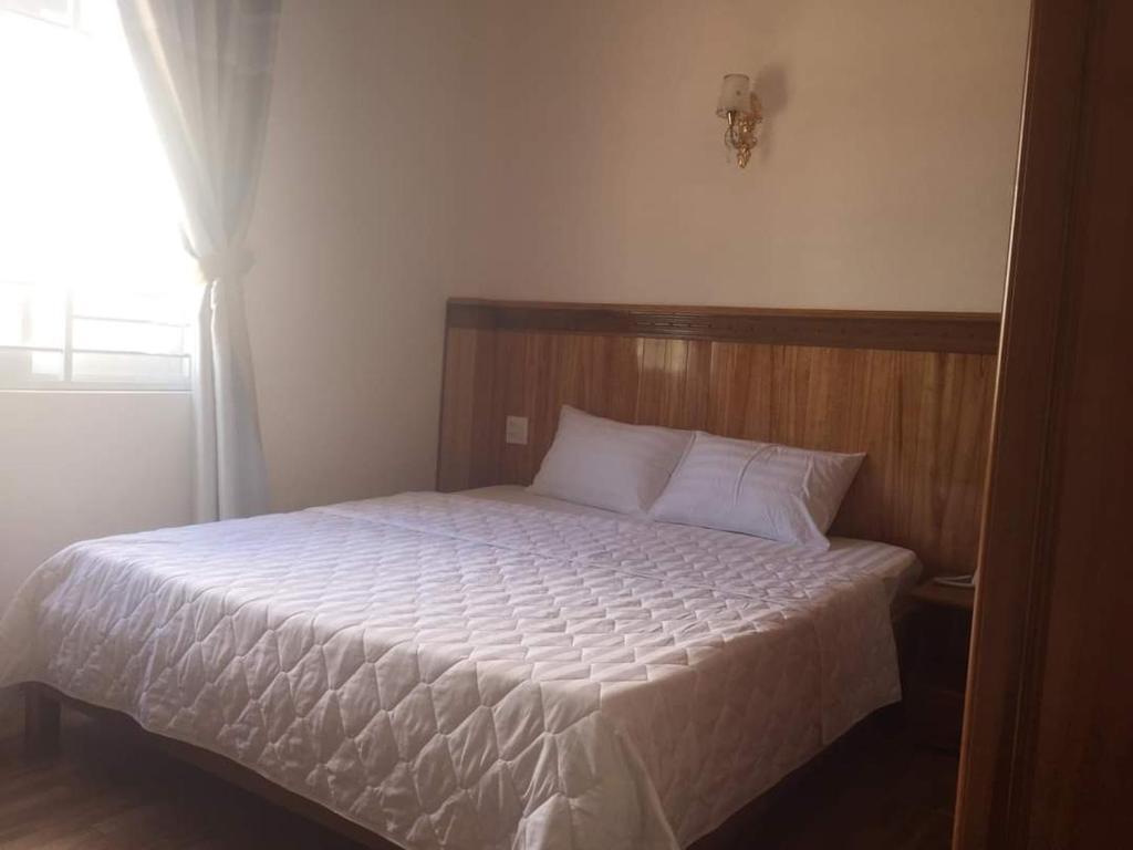 De Dang (1)Kbang的一间卧室配有一张带白色床单的床和一扇窗户。