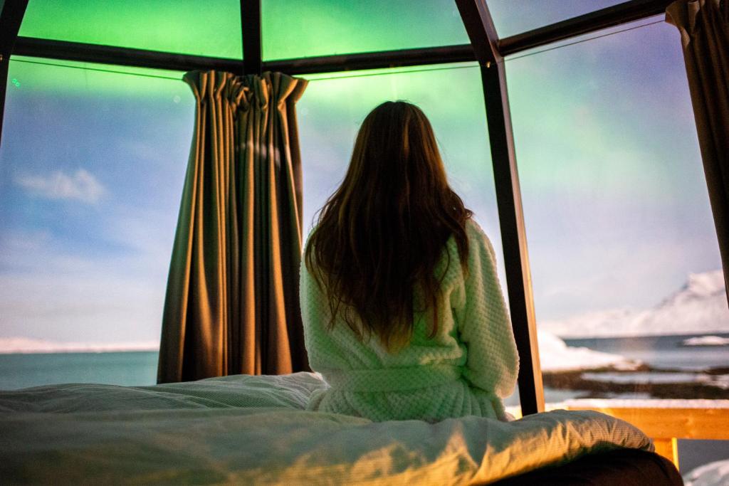 努克Aurora Hut by InukTravel的坐在床上看着窗外的女人