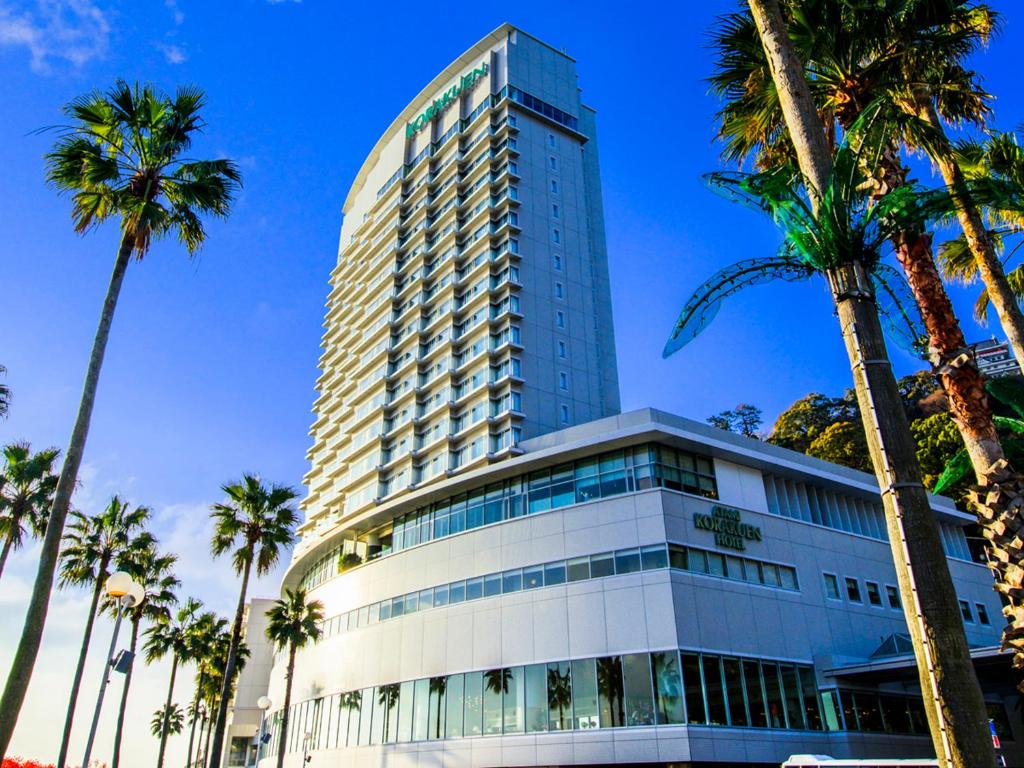 热海热海后乐园酒店(Atami Korakuen Hotel)的一座高大的建筑,前面有棕榈树