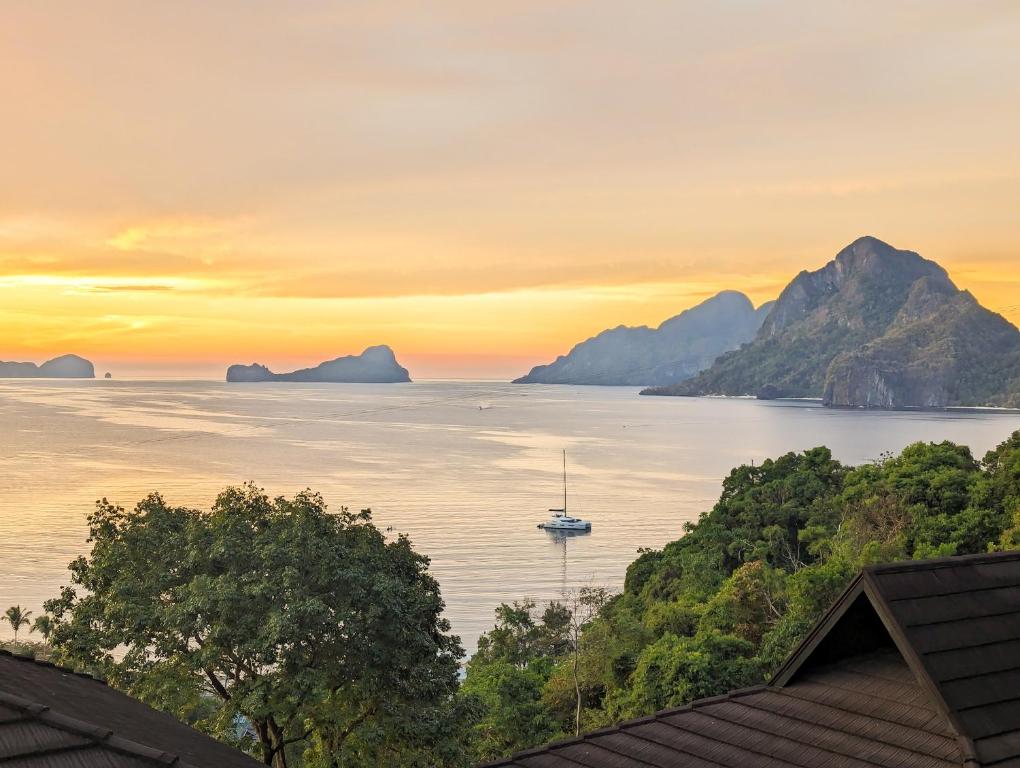 爱妮岛Perch El Nido's Seaview Villas Marimegmeg Beach的日落时分在水中与山脉一起航行的船只