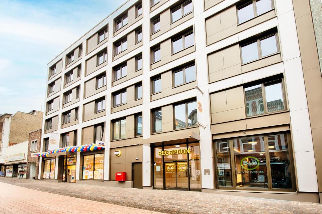 亚琛B&B Hotel Aachen-City的街上一座白色的大建筑,有商店