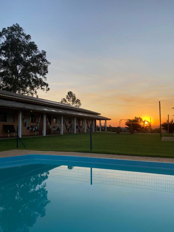 圣代佩德罗Pousada San Pietro - 2 km Thermas的一座游泳池位于一座享有日落美景的房屋前