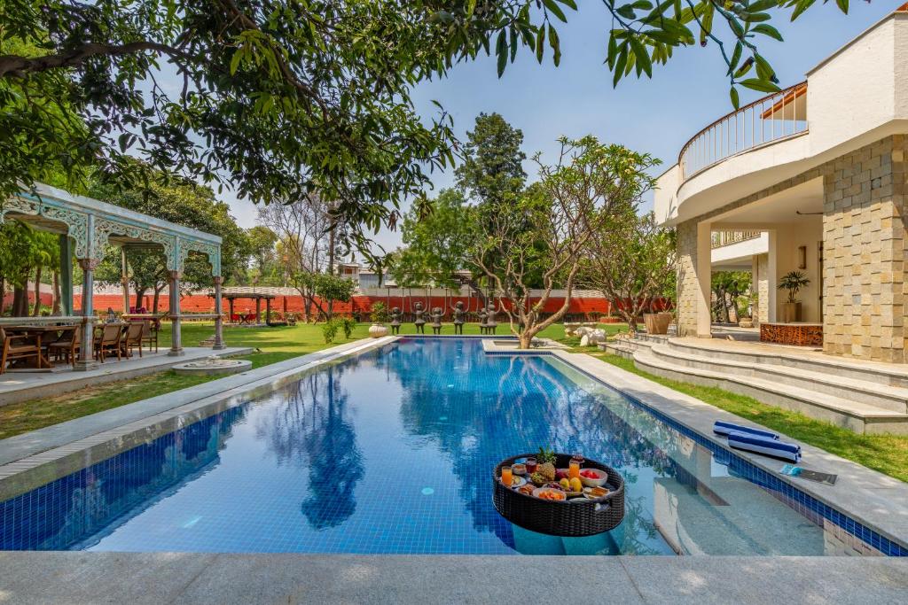 新德里Elivaas Oasis Luxury 6BHK with Pvt Pool, Sainik Farm New Delhi的一座游泳池,旁边是一所房子,里面放着一碗水果