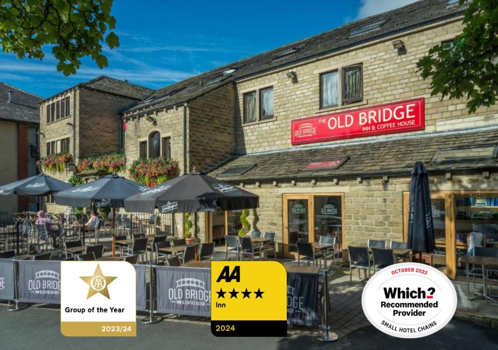 霍姆弗斯The Old Bridge Inn, Holmfirth, West Yorkshire的一座古老的砖砌建筑,前面设有桌子和遮阳伞