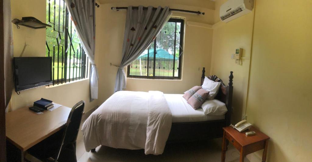 坦噶CBA Hotel的一间卧室配有一张床、一张书桌和两个窗户。