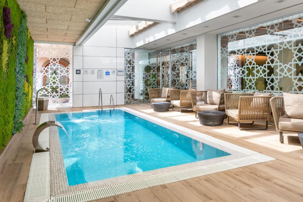 塞维利亚加泰罗尼亚吉拉达酒店的酒店大堂的游泳池,配有椅子和桌子