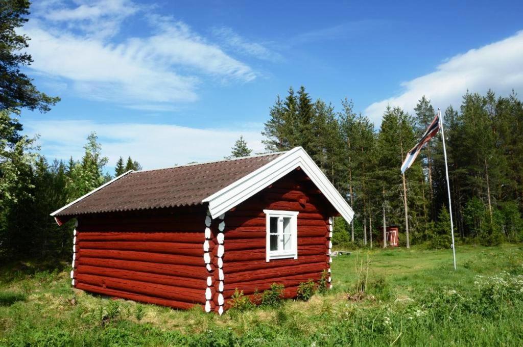 LjørdalHytte fra 1721 uten internett, strøm, vann - men med rødmalt utedo的一块带旗帜的场地上的红色小舱