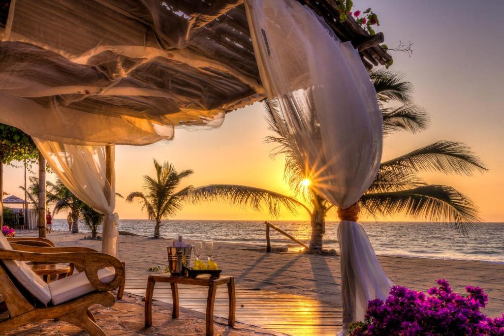 卡诺阿斯德蓬萨尔Yemaya Boutique Hotel en Canoas的海滩上的日落,配有桌椅