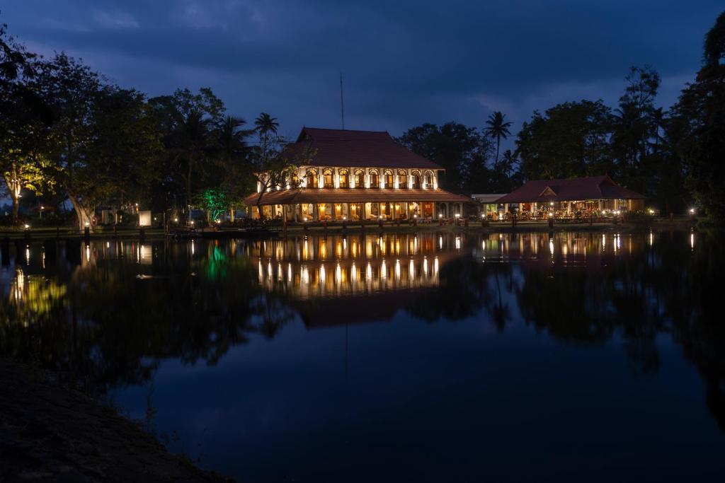 库玛拉孔Taj Kumarakom Resort and Spa Kerala的一座在夜间水面上灯亮的大建筑