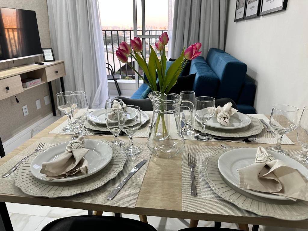 圣保罗Apartamento novo decorado com sacada e linda vista da Cidade的餐桌,带盘子和玻璃杯,鲜花