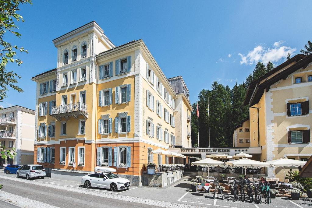 锡尔斯玛丽亚雪绒花瑞士品质酒店的城市街道上一座黄色建筑,配有桌子和遮阳伞