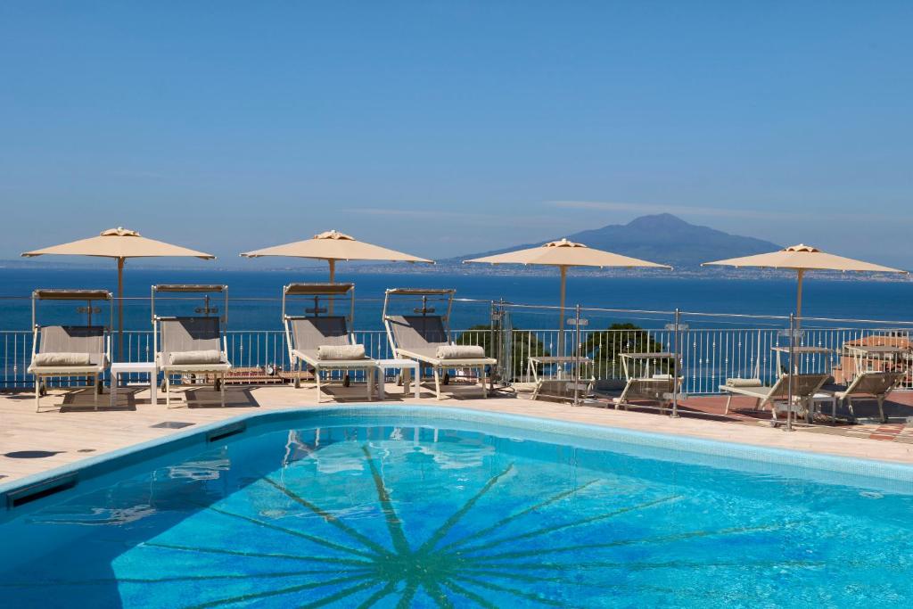 索伦托德拉维尔大酒店的一个带椅子和遮阳伞的游泳池以及大海
