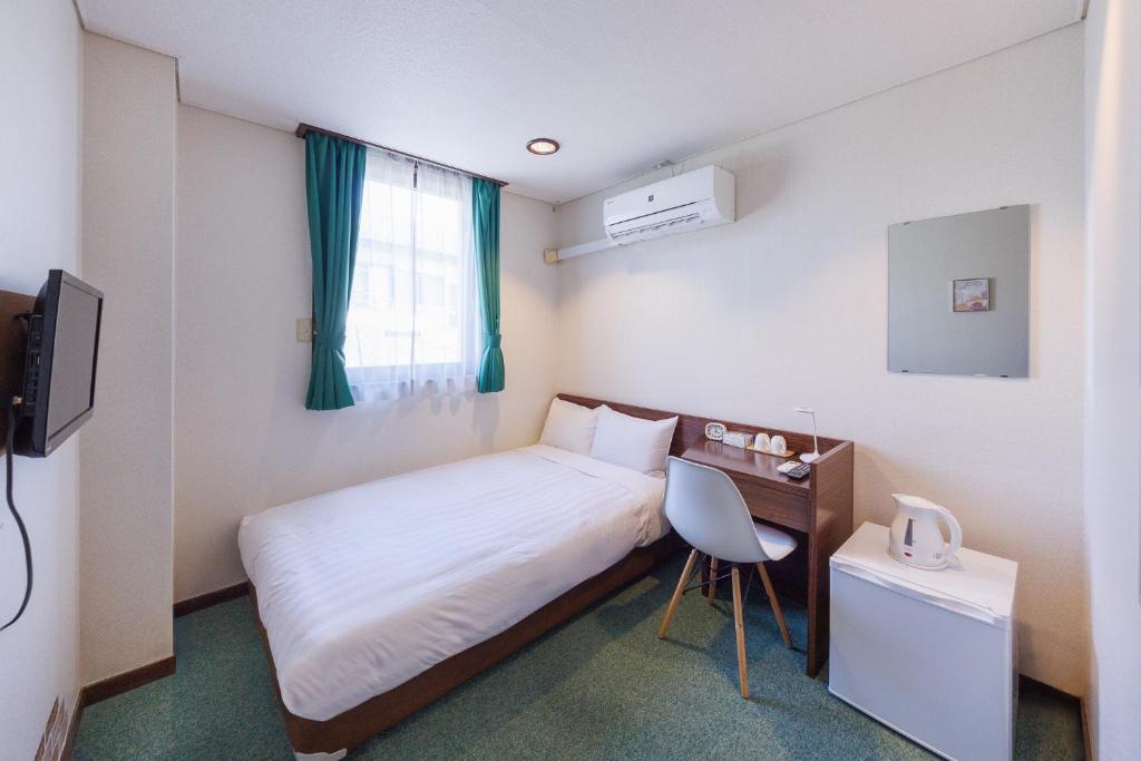 日立市ホテルノマド日立的一间卧室配有一张床、一张书桌和一个窗户。