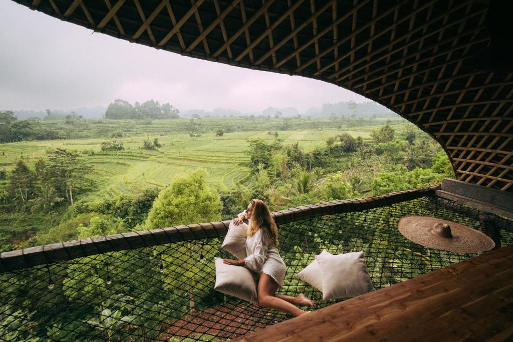 SelatCamaya Bali - Magical Bamboo Houses的坐在阳台上的女人用手机说话
