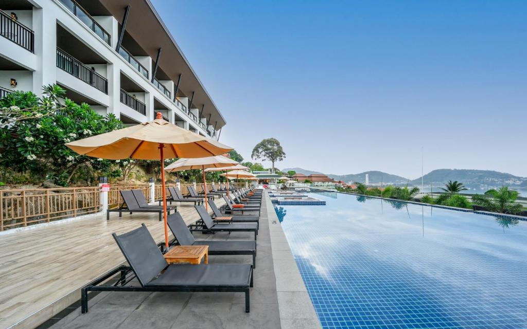 芭东海滩Andamantra Resort and Villa Phuket - SHA Extra Plus的一座带椅子和遮阳伞的游泳池位于大楼旁