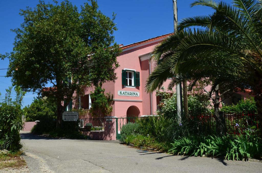 木洛希尼Villa Katarina Mali Lošinj的一座粉红色的建筑,前面有一棵棕榈树