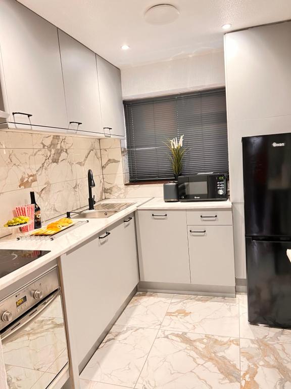 巴塞尔顿Luxury 2-Bedroom House - Smart Home - Basildon Serviced Accommodation - 6Mins Walk To Basildon Town Centre, Hospital & Train Station的厨房配有白色橱柜和黑色冰箱。