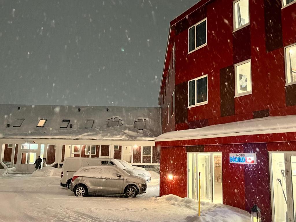 努克Hotel Nordbo的雪中红色建筑前的汽车