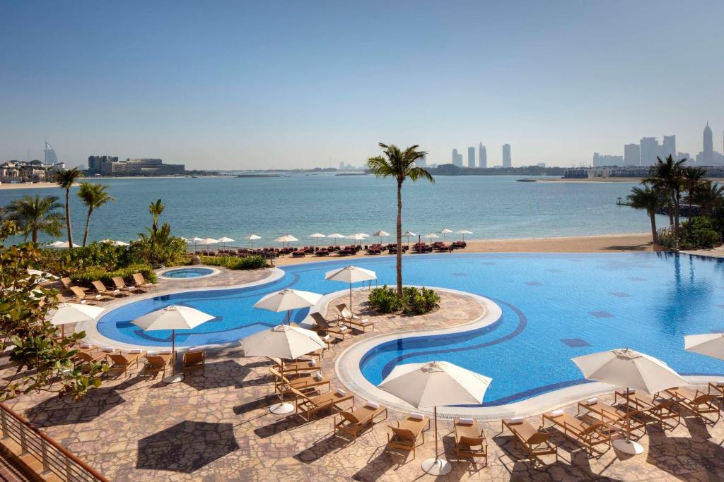 迪拜Andaz by Hyatt – Palm Jumeirah的毗邻大海的带椅子和遮阳伞的游泳池